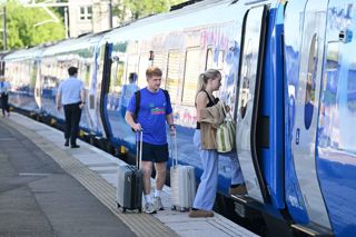 A man and a woman with suitcases board a blue Lumo train at Stirling station. LUMO.