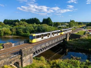 Manchester has been favoured by the government, with transport plans including a Metrolink extension to Stockport and new tram stops. Longer two-car trams to reduce the double-heading of the ‘M5000’ Bombardier/Alstom units has also been suggested locally. In such a formation, Metrolink Trams 3046 and 3047 cross the River Irwell on August 11 2004, approaching Radcliffe with a Bury to Altrincham service. TOM MCATEE.