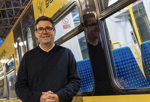 Andy Burnham in front of a yellow Bee Network-liveried train. TRANSPORT FOR GREATER MANCHESTER.