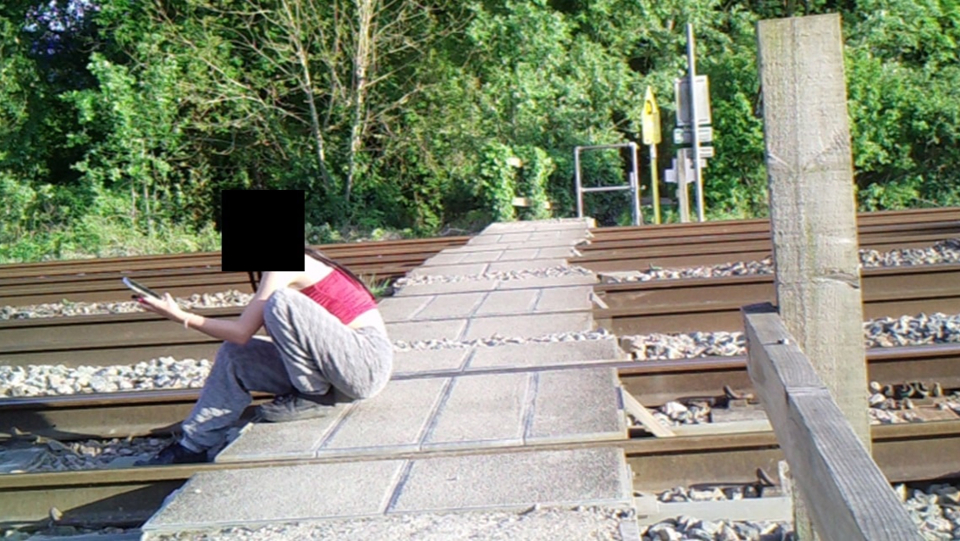 A teenager sits with her back to traffic at Wantage Road level crossing near Didcot. NETWORK RAIL.
